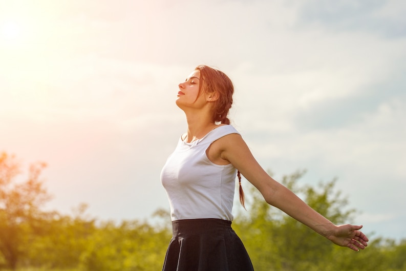 beautiful girl enjoying sun with her arms outstretched field against sky